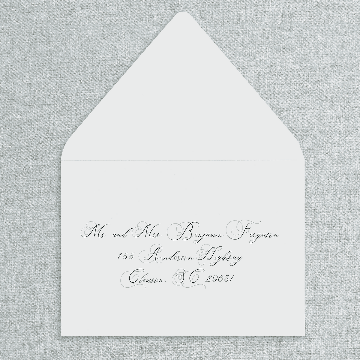 White envelope with black text of your wedding guests' addresses on a gray textured background.