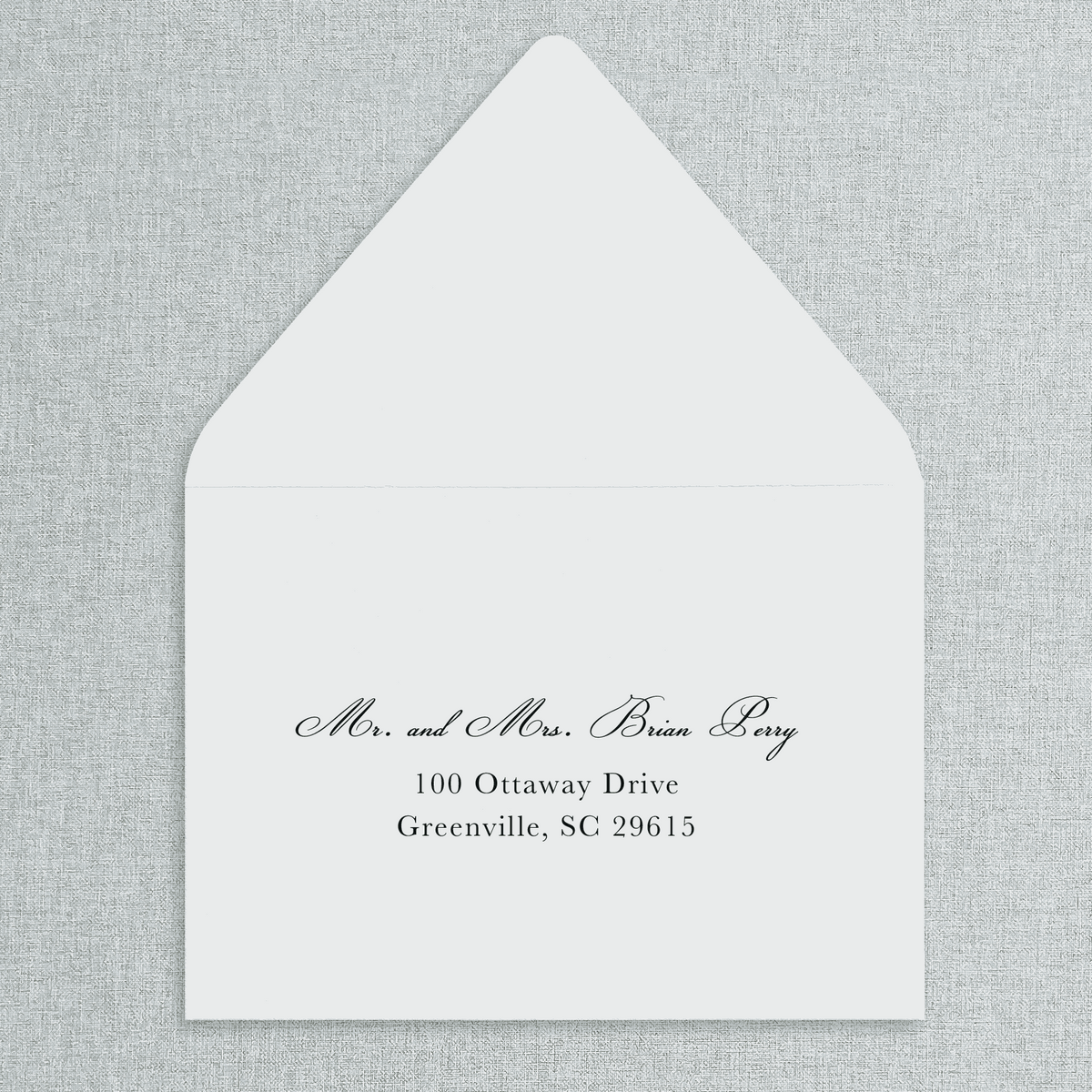 White envelope with black text of your wedding guests' addresses on a gray textured background.