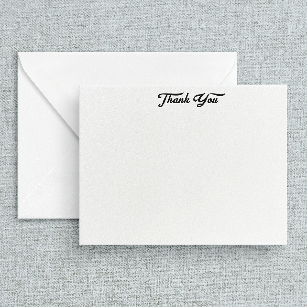 A simple letterpress print 'Thank You' note on a white background with black cursive text, accompanied by a white envelope.