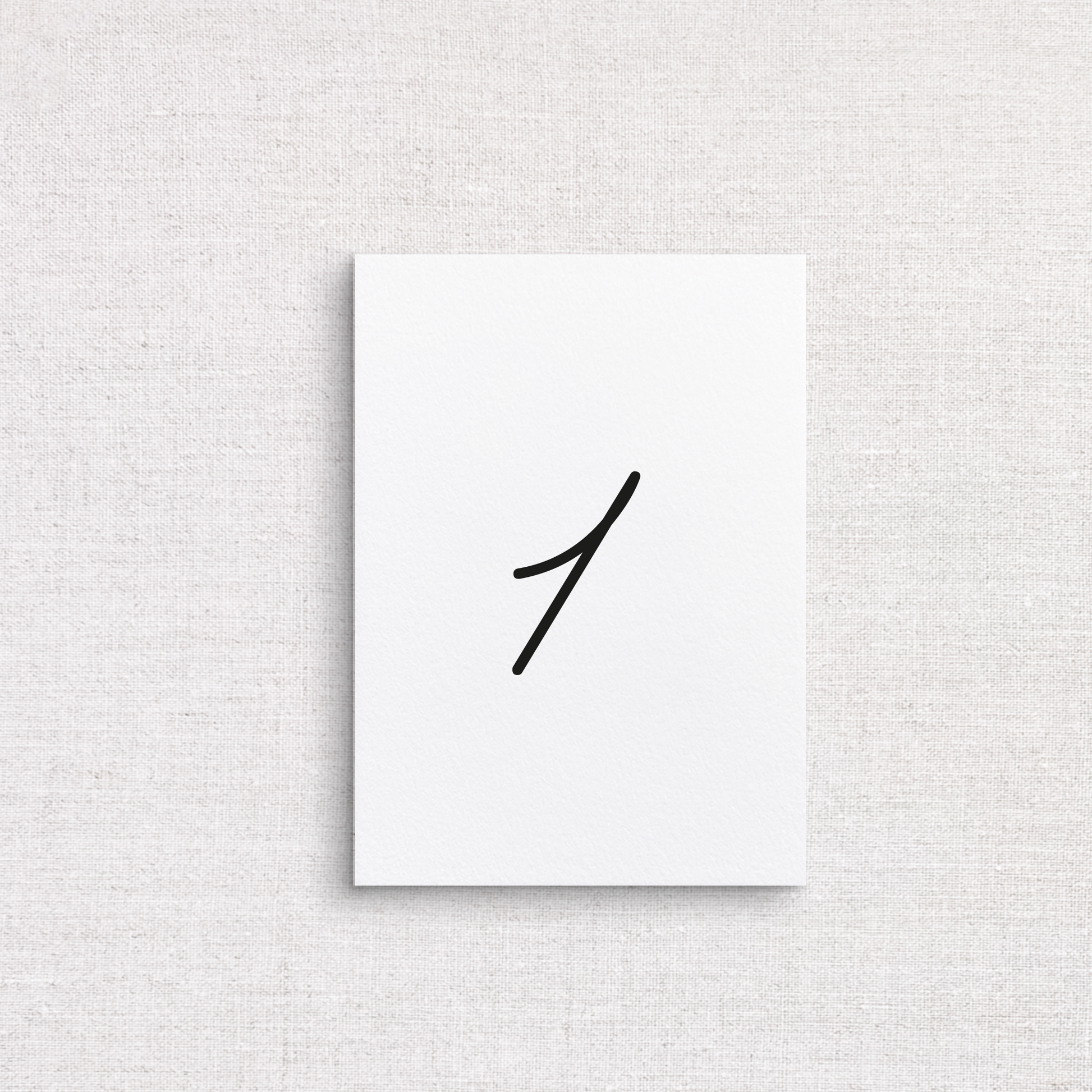 A minimalist wedding table number with single black handwritten numeral '1' in the center, displayed against a textured light beige linen background.