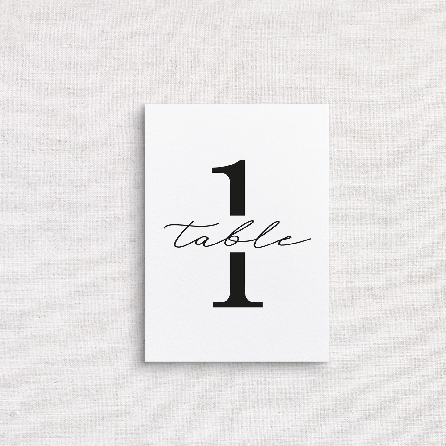 A minimalist white wedding table number print featuring the number 1 with the word 'table' in black cursive script, displayed against a light gray linen-textured background.