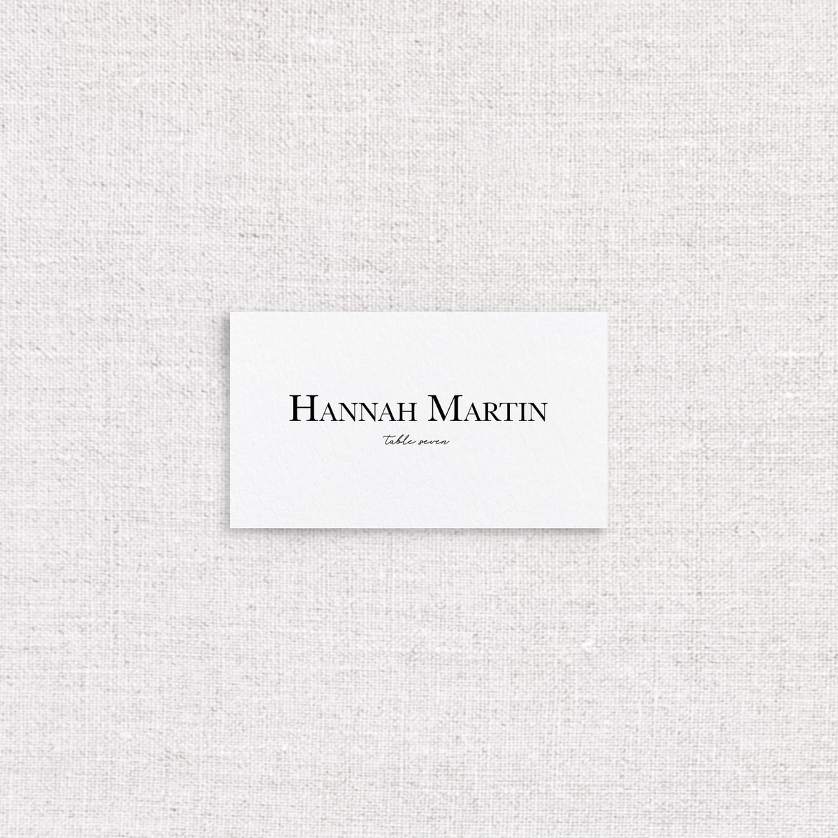 White place card with guests name in a serif font and the table number in a script font. 