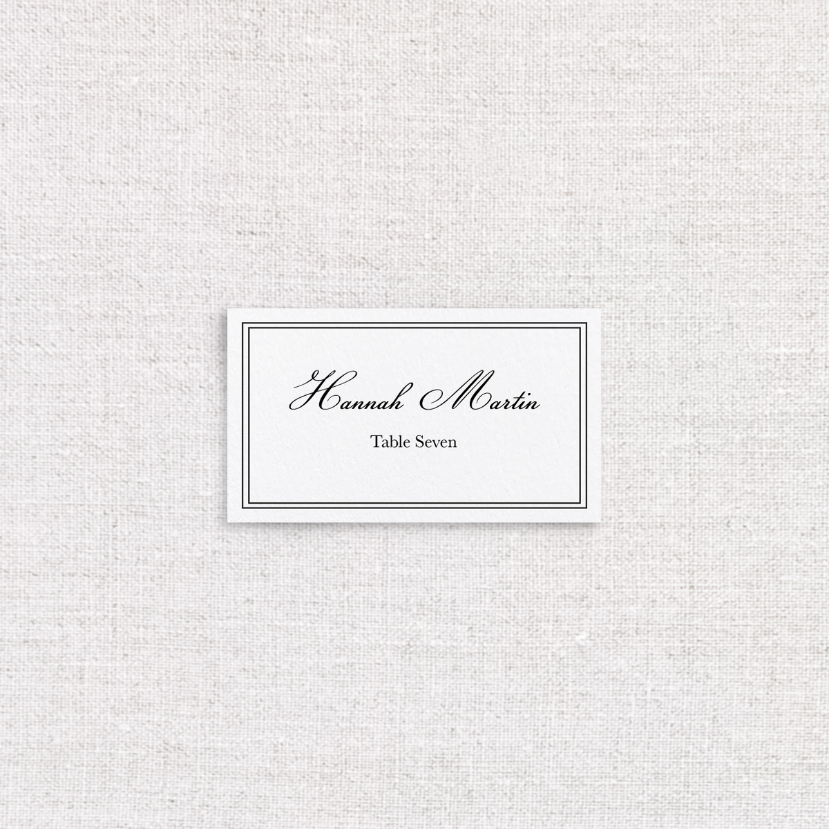 White place card with a double line border. Guests name is a traditional cursive with the table number in a serif font. 