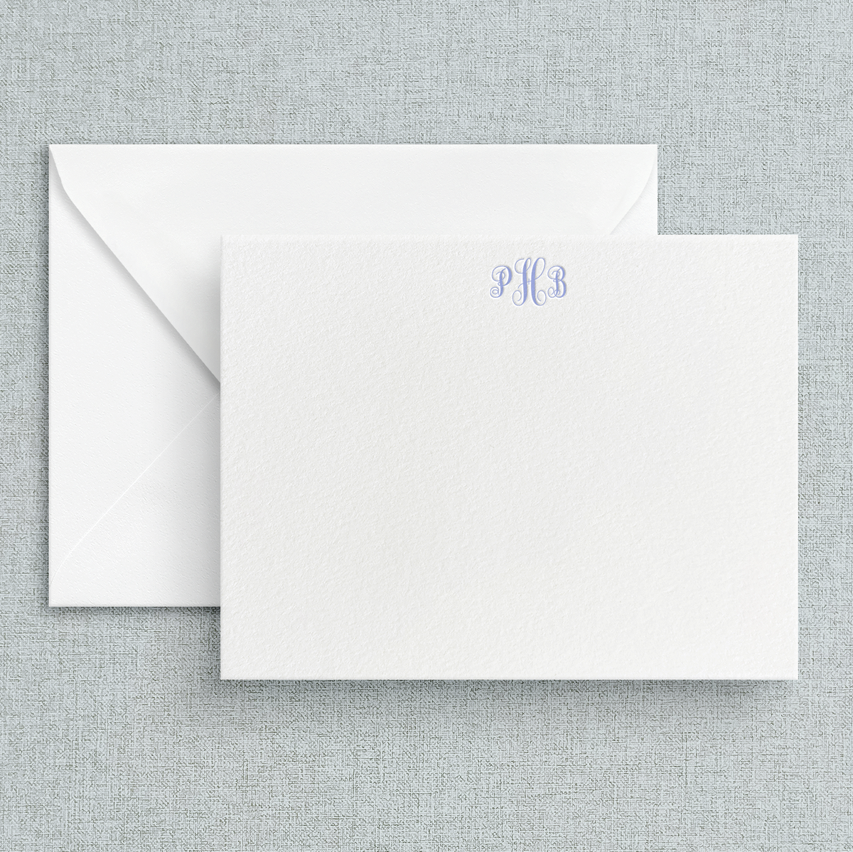 A set of custom letterpress stationery cards with a circle script monogram at the top, displayed with white envelopes.