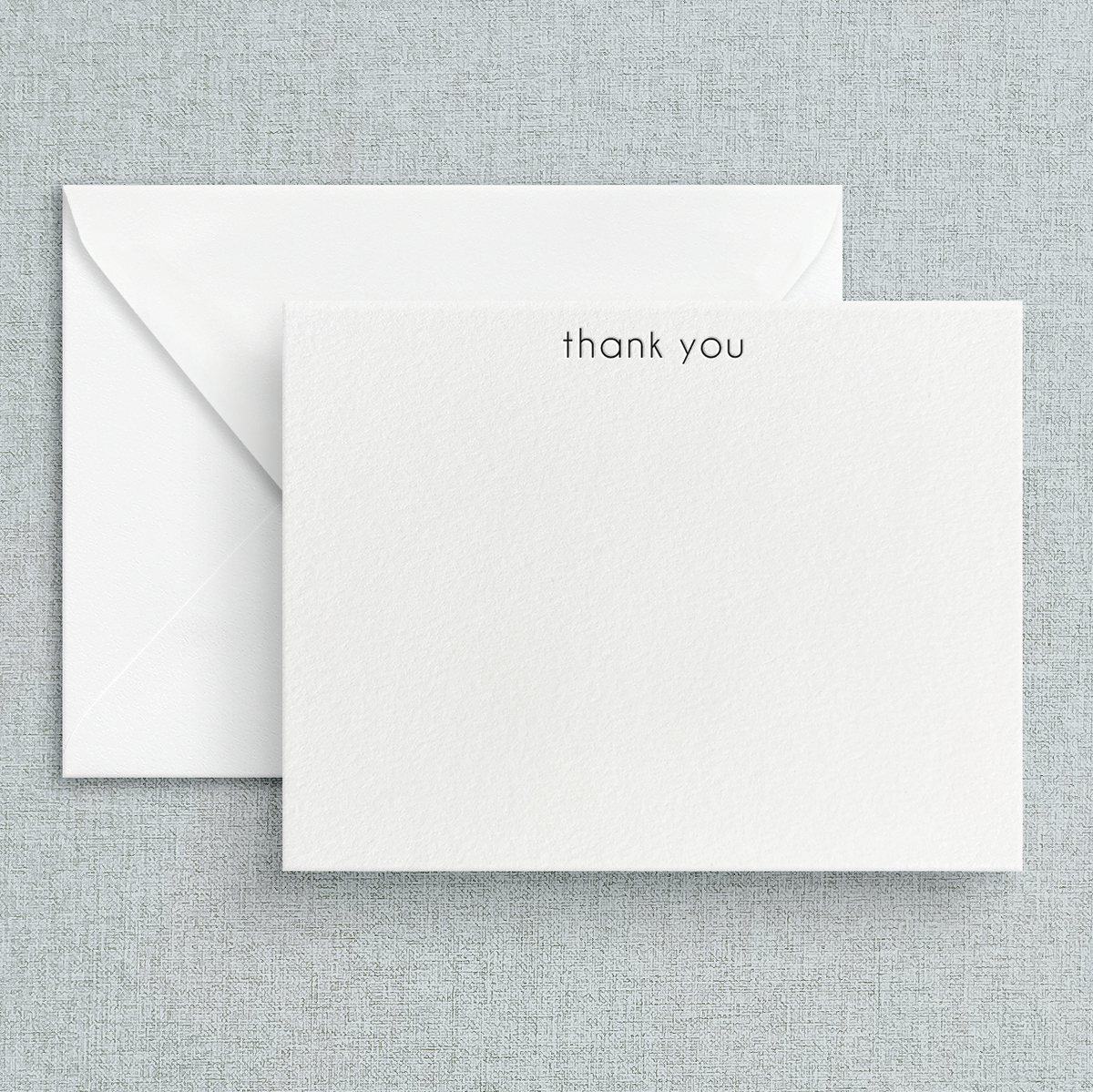A simple letterpress printed 'thank you' note printed in lowercase on a white note card, accompanied by a white envelope, set against a textured background.