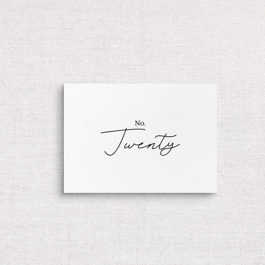 A minimalist white rectangular table number card with the words 'No. Twenty’ printed in black script and serif text, centered on a light beige linen-textured background.