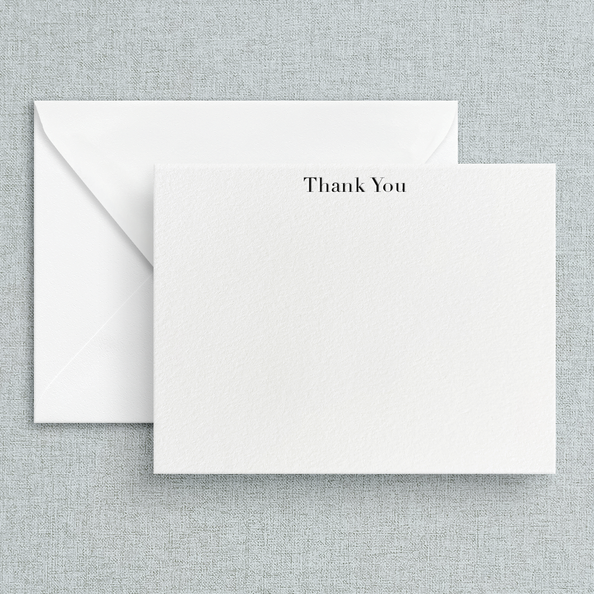 A simple letterpress printed 'Thank You' note printed in black on white cardstock, accompanied by a white envelope, set against a textured background.