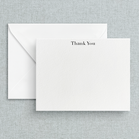A simple letterpress printed 'Thank You' note printed in black on white cardstock, accompanied by a white envelope, set against a textured background.